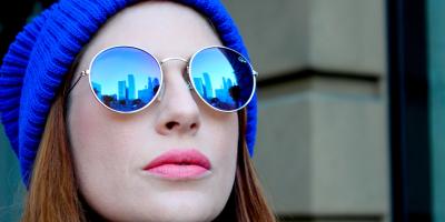 Woman wearing aviator glasses and wearing a blue beanie stares to the left of the image