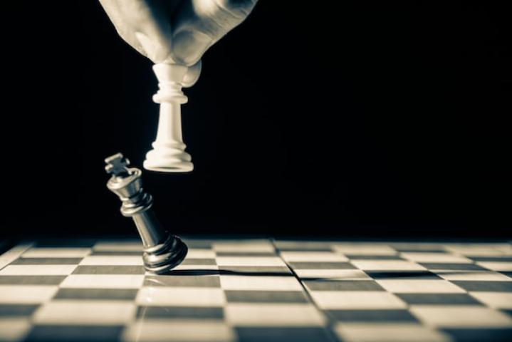 White Chess piece knocking over a black chess piece